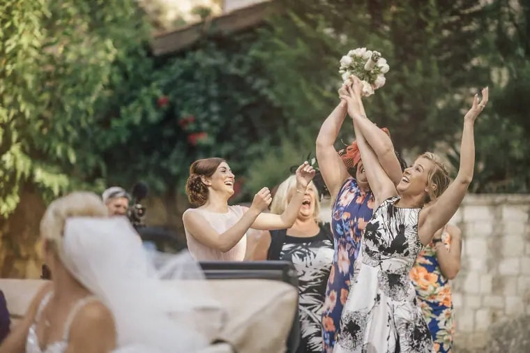 Bride throwing her bouquet as female guests reach up to catch it