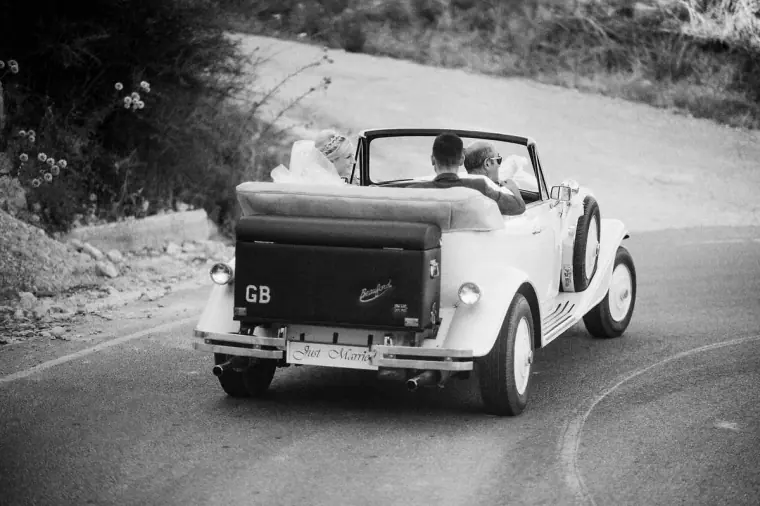 Black-and-white photo of the vintage car driving the newlyweds down a winding road