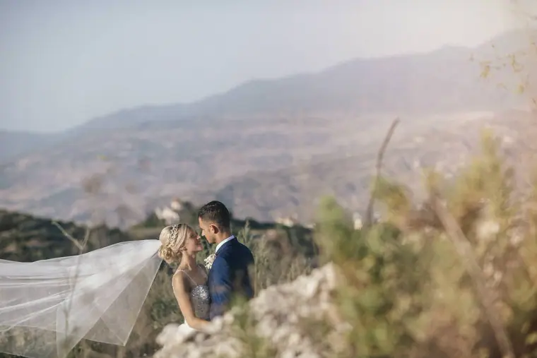 Bride and groom embracing on a hillside, her veil sweeping across the frame