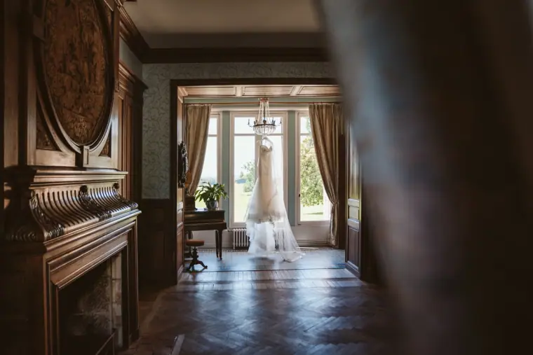 Wedding dress hanging at the end of a wood-panelled château corridor
