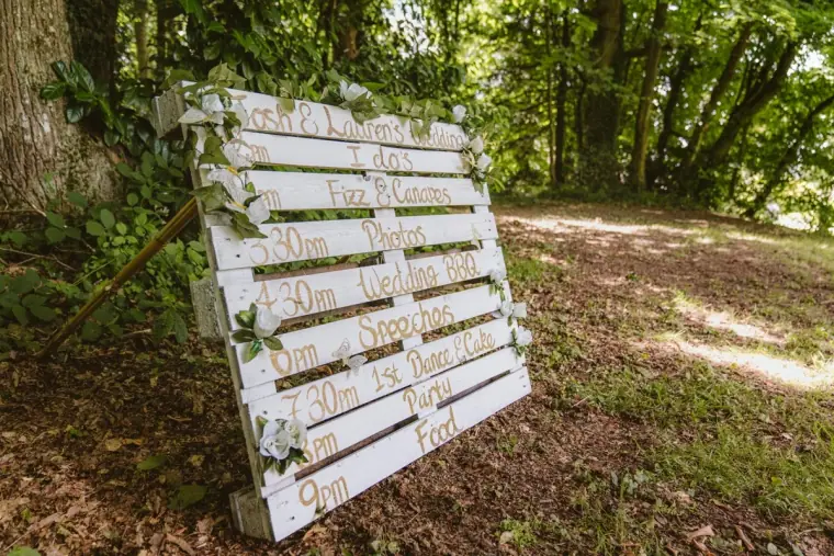 White wooden pallet seating plan propped against a tree in the woodland