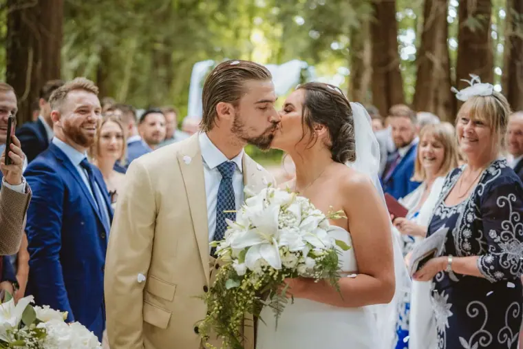 Lauren and Josh kissing amid cheering guests after their woodland ceremony