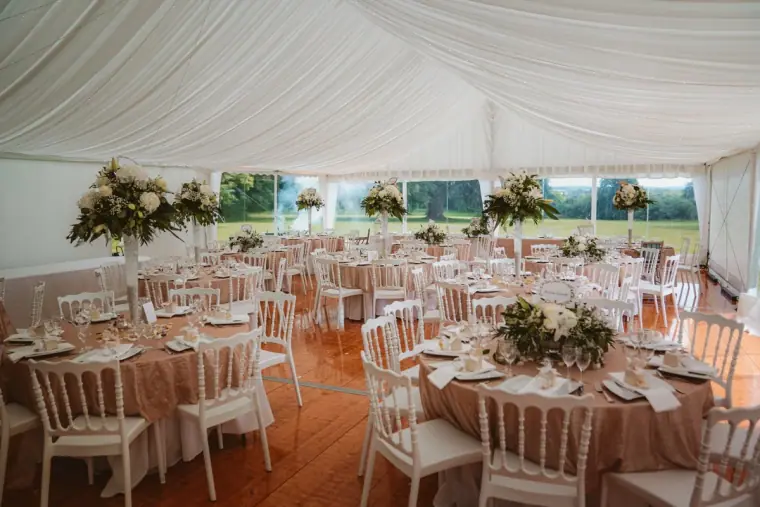 Marquee reception with round tables, white chairs and tall floral centrepieces