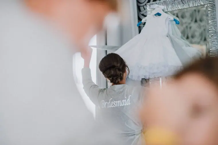 Bridesmaid in a grey robe hanging up the wedding dress