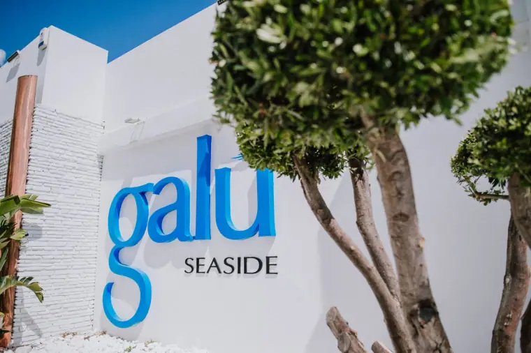 Galu Seaside sign on a white wall beside a sculpted topiary tree