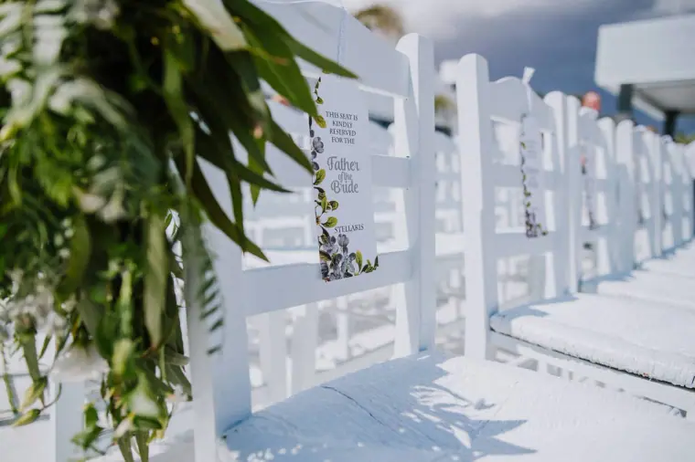 White ceremony chairs decorated with greenery and a welcome sign