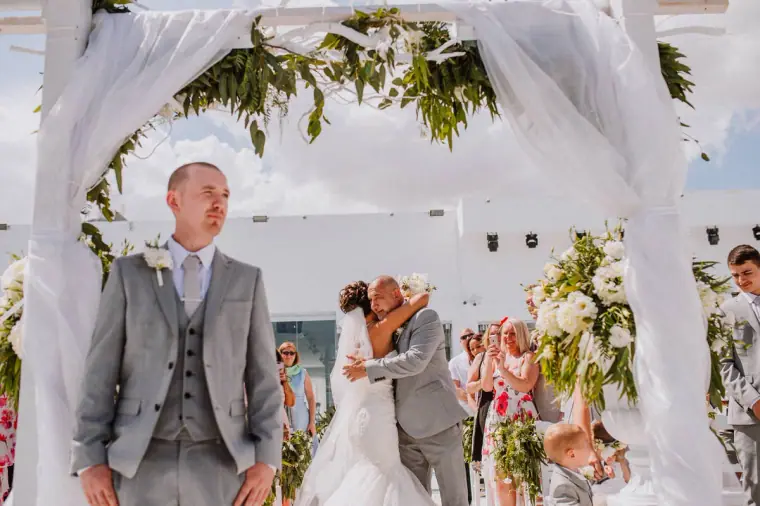 Mike waiting under the draped arch as Louise embraces her father at the end of the aisle