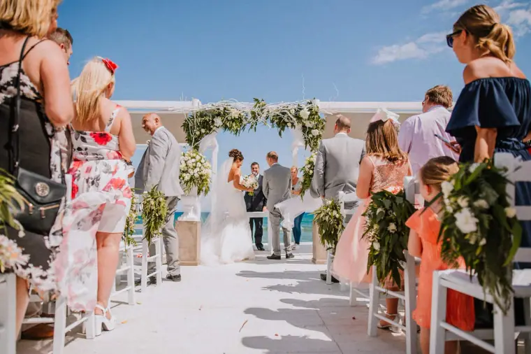 Guests watching from the aisle as the couple stand at the seaside arch