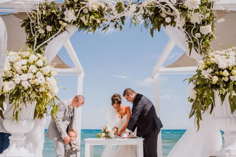 Louise and Mike signing the register under the floral arch by the sea