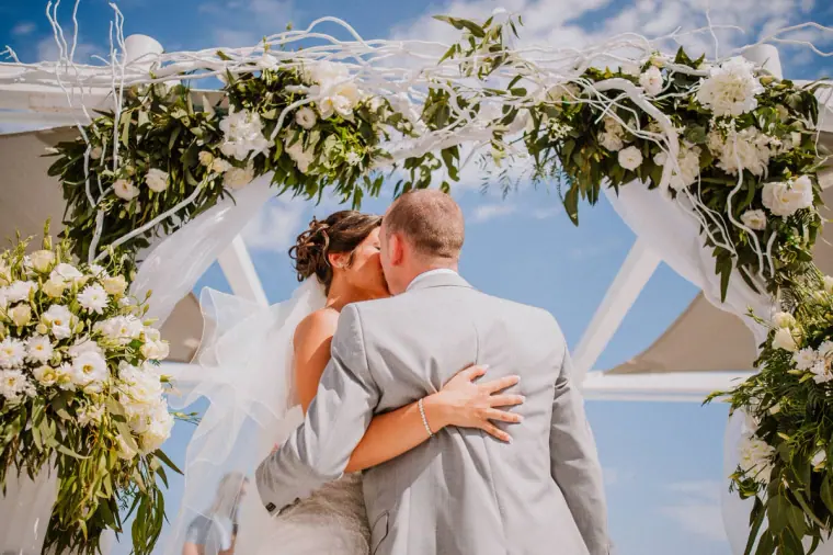 Louise and Mike's first kiss beneath the white floral arch