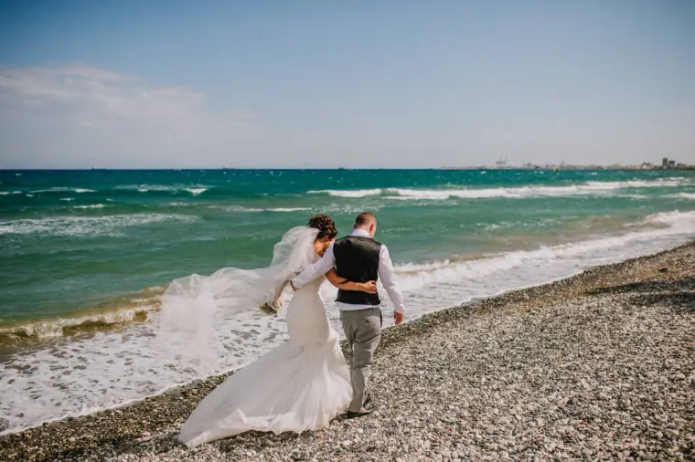 Louise and Mike walking along the shoreline, her veil streaming, at Galu Seaside, Larnaca