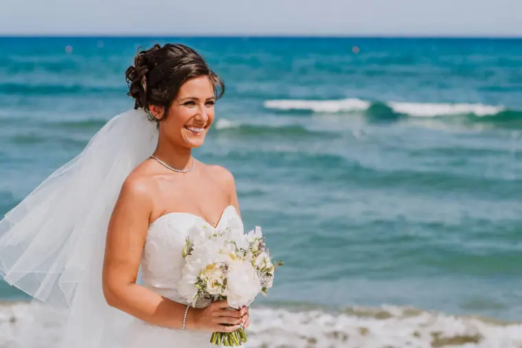 Louise smiling with her white bouquet, the turquoise sea behind her