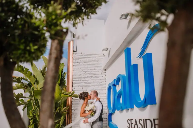 Louise and Mike kissing beside the blue Galu Seaside sign