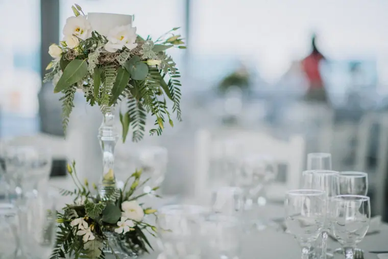 Tall centrepiece of white flowers and greenery above glassware