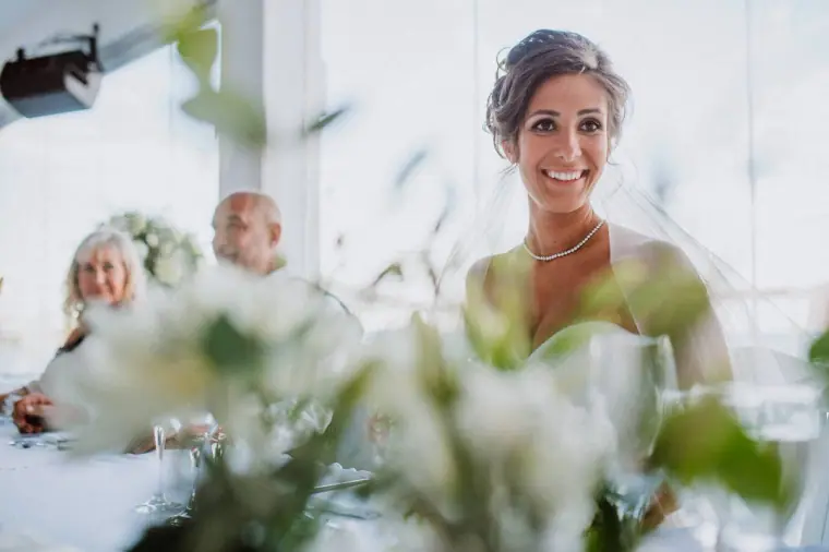 Guest in a green dress smiling at the reception behind white flowers