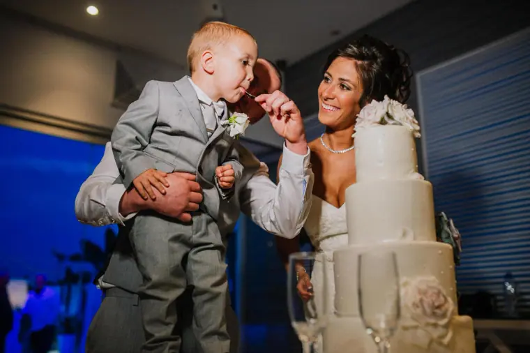 Mike lifting the young pageboy beside the wedding cake as Louise laughs