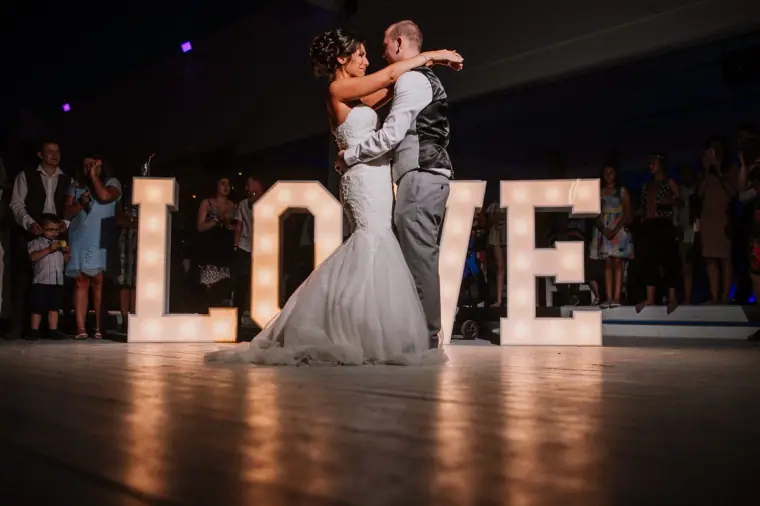 Mike twirling Louise during their first dance by the illuminated LOVE letters