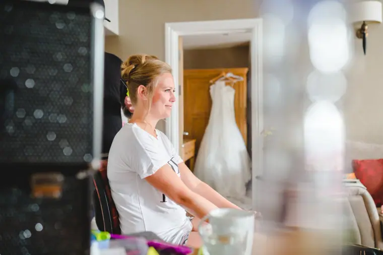 Bride relaxing in a white T-shirt, her wedding dress hanging behind