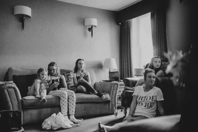 Black-and-white photo of the bridal party relaxing on sofas while getting ready