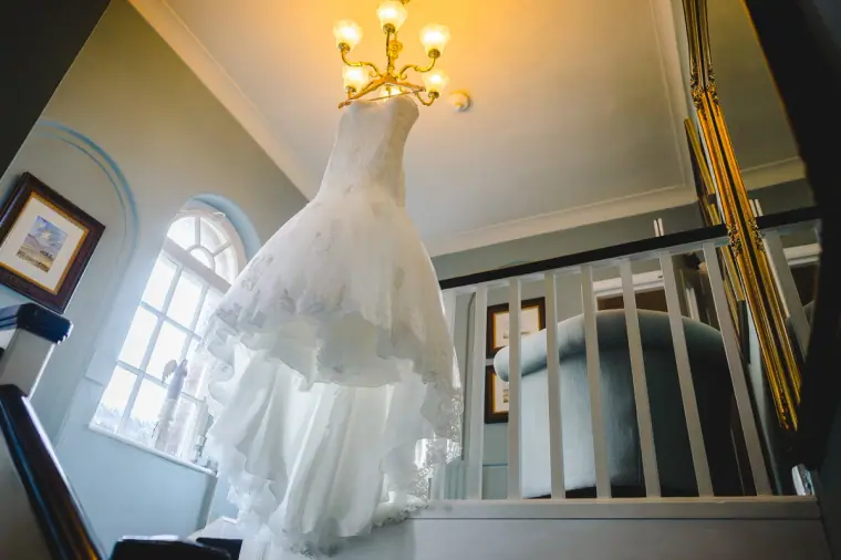 Wedding dress hanging beneath a chandelier at the top of a staircase