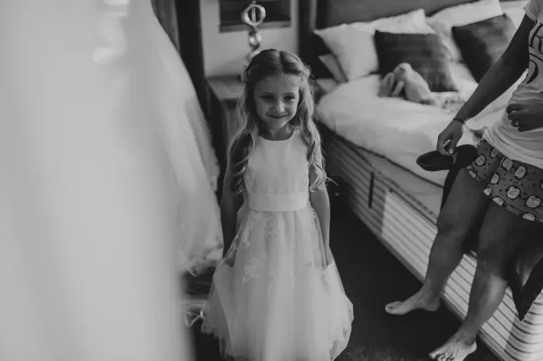 Black-and-white photo of a young bridesmaid in a white dress waiting by the bed