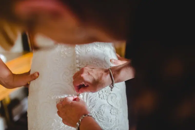 Close-up of hands fastening the buttons on the back of the lace gown