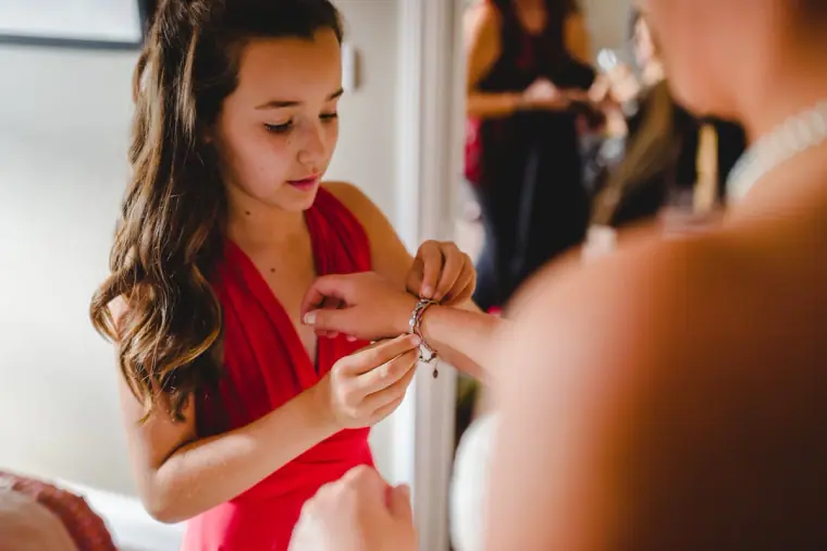 Young bridesmaid in red fastening the bride's bracelet