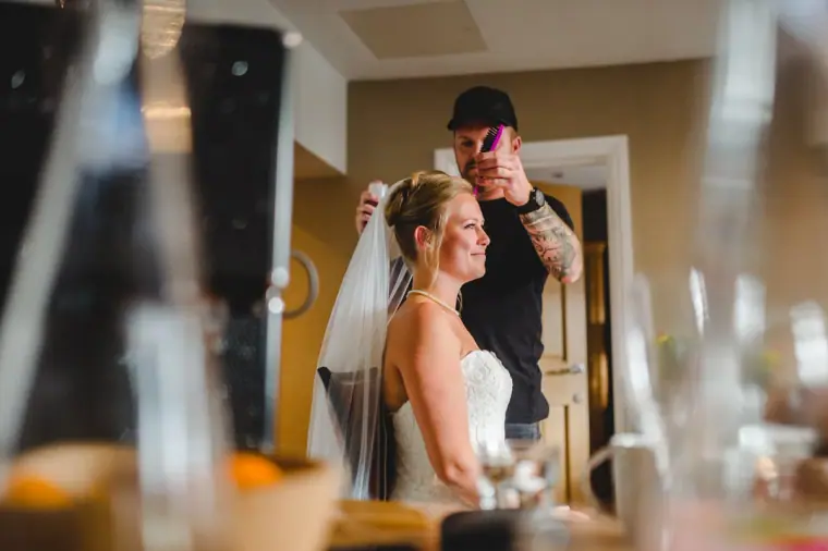 Bride in her veil being photographed in the suite by a man with a phone