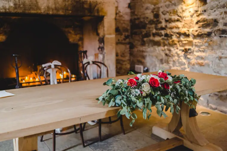 Wooden signing table with a red rose and greenery arrangement before a stone fireplace