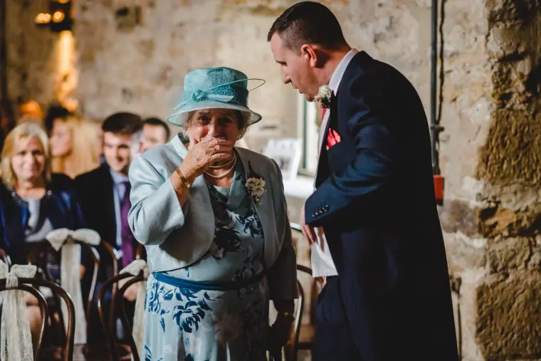 Guest in a blue hat wiping away a tear as the groom passes