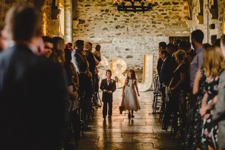Young bridesmaid and pageboy walking down the aisle between guests