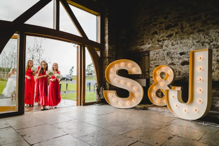 Bridesmaids in red entering the barn past giant light-up S&J letters