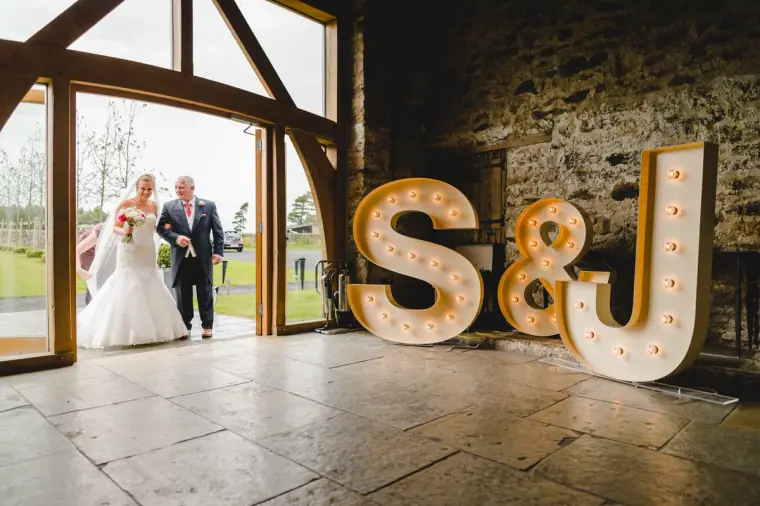 Bride and her father arriving through the glass doors beside the S&J letters