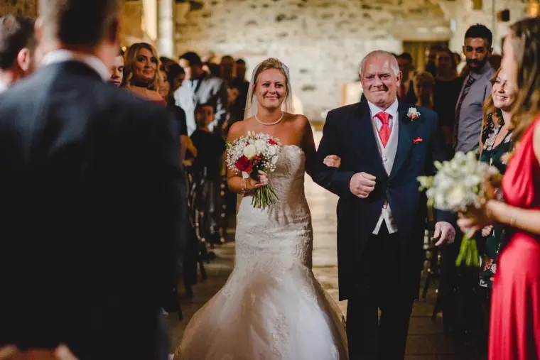 Father walking the bride down the aisle as guests look on