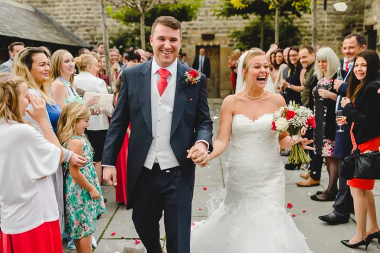 Sonny and Jo walking hand in hand through a line of smiling guests