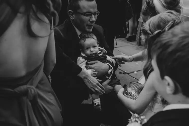 Black-and-white photo of a guest holding a baby among the crowd