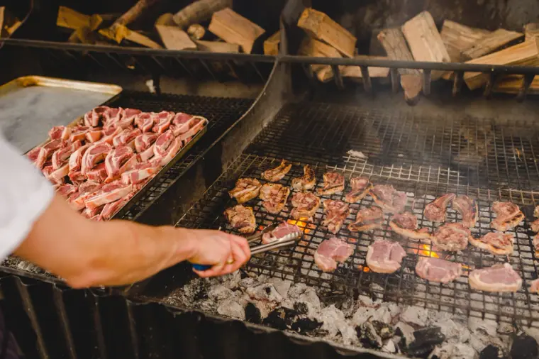 Close-up of meat sizzling on the barbecue grill with logs stacked behind