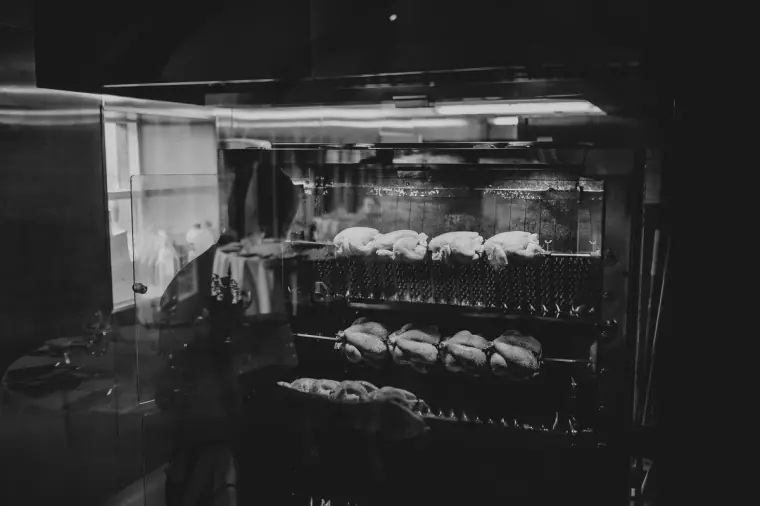 Black-and-white photo of chickens roasting on spits in the barn kitchen