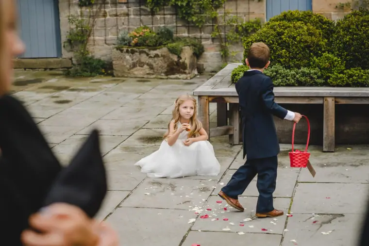 Young bridesmaid sitting on petals as a pageboy carries a red basket