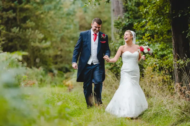 Groom leading the laughing bride along a forest track
