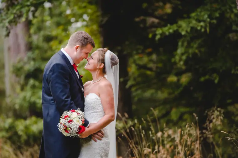 Sonny and Jo touching foreheads among the trees, her red and white bouquet in hand