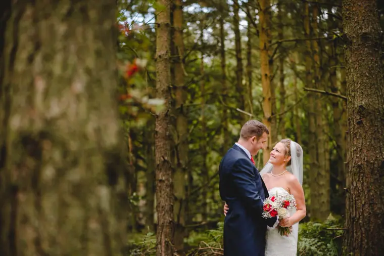 Couple embracing between tall pine trunks in the woods