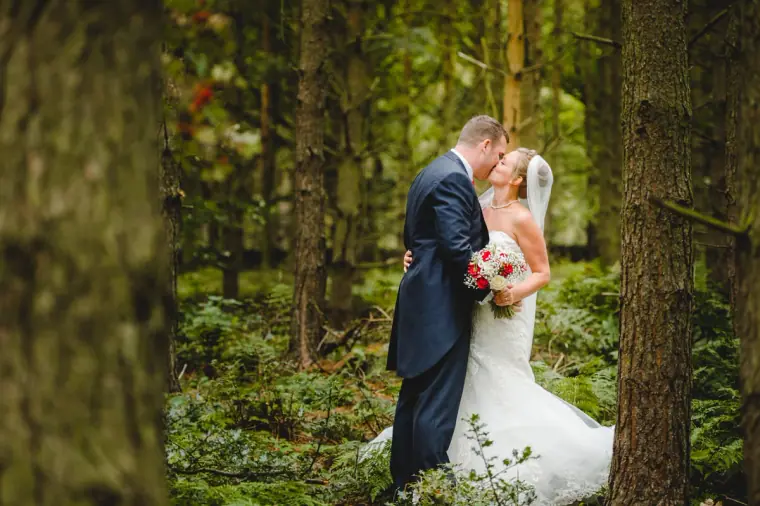Groom kissing the bride in a fern-filled pine forest