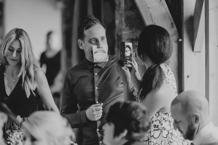 Black-and-white photo of guests filming and laughing during the reception