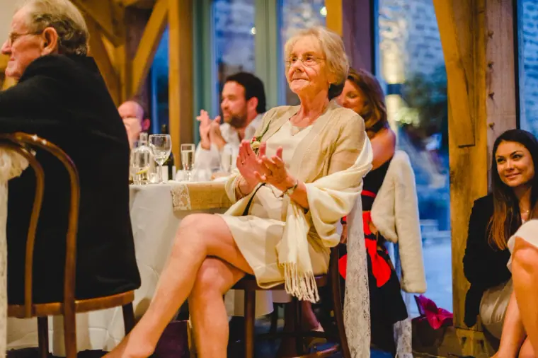 Older guest clapping and smiling in her chair at the reception