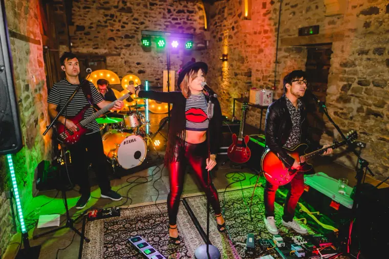 Live band performing with a singer in red trousers and two guitarists