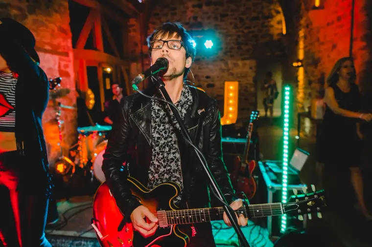 Guitarist singing into a microphone under coloured lights