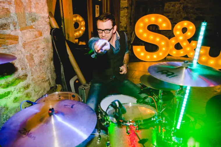 Drummer pointing at the camera beside the illuminated S&J letters