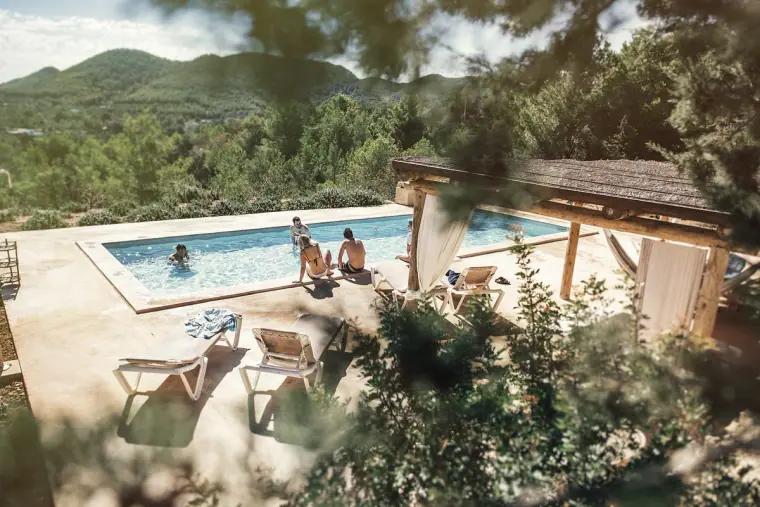 Guests relaxing by a villa pool among pine-covered Ibiza hills