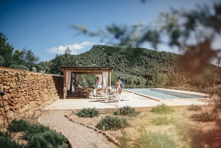 Stone-walled villa terrace with a pergola and pool set against green hills